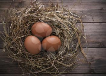 Eggs in hay nest on old wooden table background, top view