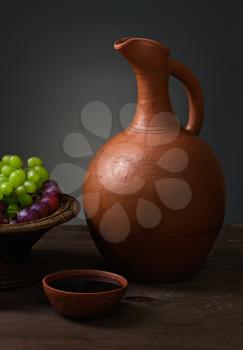 red wine with grapes and a pitcher on a wooden table
