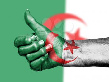 Old woman with arthritis giving the thumbs up sign, wrapped in flag pattern, Algeria