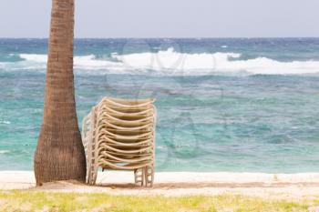 Stack of beach chairs under palm tree on idyllic tropical white sand beach