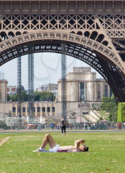 PARIS - July 27, 2013: Tourist is sunbathing on July 27, 2013 near the Eiffel tower in Paris, France. The tower is an 1889 iron lattice tower which stands at 324 meters. PARIS, July 27, 2013
