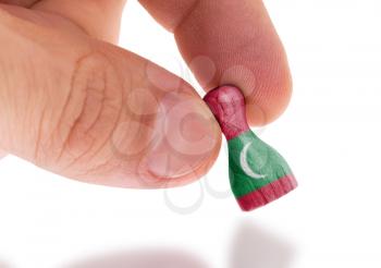 Hand holding wooden pawn with a flag painting, selective focus, Maldives