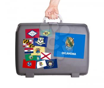 Used plastic suitcase with stains and scratches, stickers of US States, Oklahoma