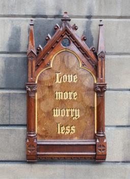 Decorative wooden sign hanging on a concrete wall - Love more worry less