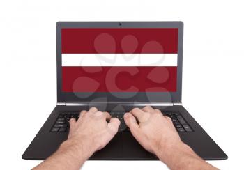 Hands working on laptop showing on the screen the flag of Latvia