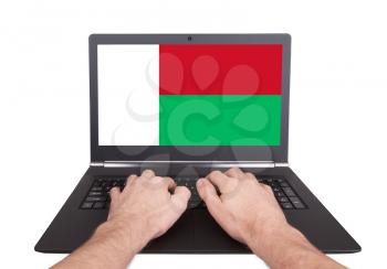 Hands working on laptop showing on the screen the flag of Madagascar