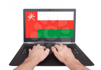 Hands working on laptop showing on the screen the flag of Oman