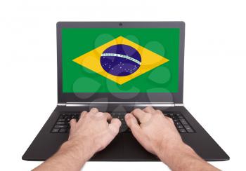 Hands working on laptop showing on the screen the flag of Brazil