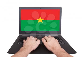 Hands working on laptop showing on the screen the flag of Burkina Faso