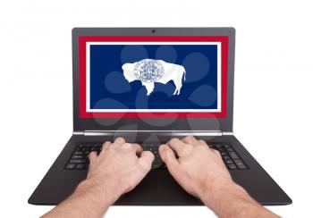 Hands working on laptop showing on the screen the flag of Wyoming