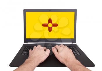 Hands working on laptop showing on the screen the flag of New Mexico
