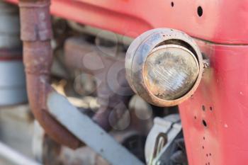 Old tractor face, red, rusty an dented, selective focus on it's light