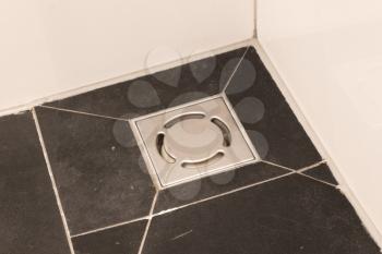 Metal drain hole in the tiled floor of a shower in bathroom