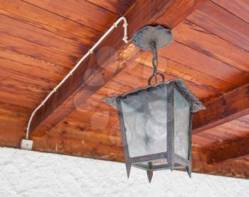 Vintage looking metal lantern with modern lamp inside hanging from the wooden ceiling