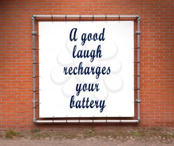 Large banner with inspirational quote on a brick wall - A good laugh recharges your battery