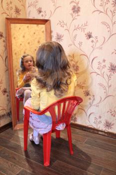litte girl makes up her face before a mirror