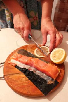 image of hand cuts slices of a red fish and lemon