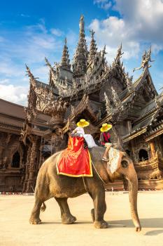 Tourists ride elephant around the Sanctuary of Truth in Pattaya, Thailand in a summer day