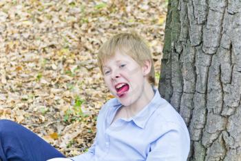Boy sitting near tree and put out tongue