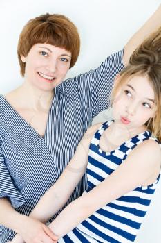 Mother and daughter playing with blond long hair near white wall