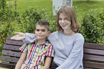 Brother and sister are sitting on bench in summer