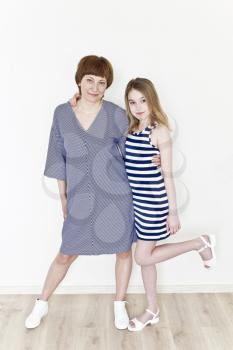 Happiest mother and daughter playing near white wall in striped clothes