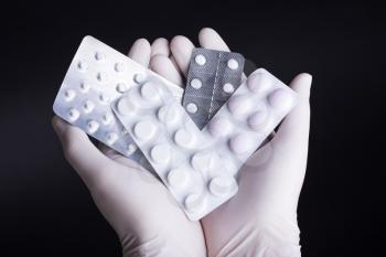 Male hand in glove holding pills in blisters on dark background. Square format.