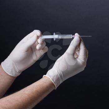 Male hands in latex gloves holding a syringe on dark background