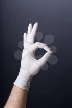 Male hand in latex glove OK sign on dark background