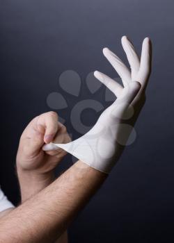 Male hands in golves. Doctor or nurse putting on latex gloves. Sanitary, healthcare, medical clothing. Dark background