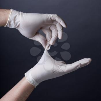 Male hands in golves. Doctor or nurse putting on latex gloves. Sanitary, healthcare, medical clothing. Dark background