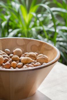 Nuts in wooden bowl on a bulrap tablecloth. Green garden background. Country style. Natural foods, vegan supplement, healthy fat source. Almonds, walnuts, hazelnuts.