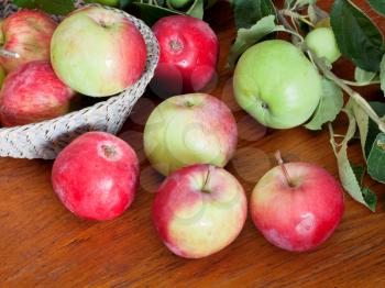 red and green apples with leaves in basket on wooden table close up