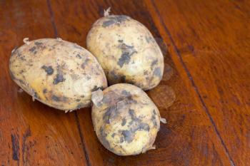 three raw potatoes on brown wooden table