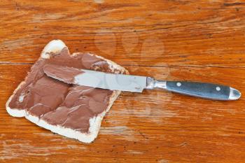 sweet sandwich from fresh toast with chocolate spread, table knife on wooden table