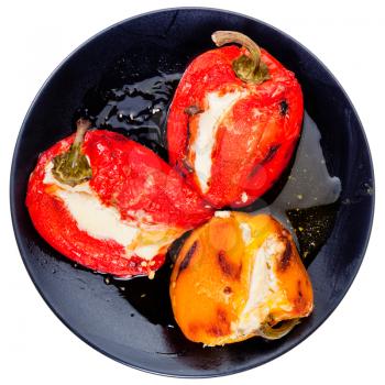 top view of roasted peppers with goat cheese on black plate isolated on white background