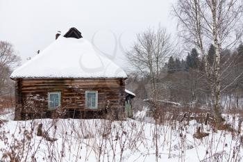 snow covered wooden rustic house in country in grey winter day