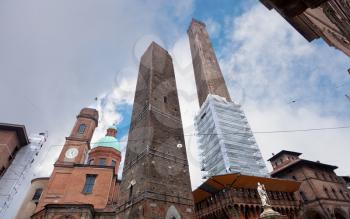 palace and two towers and statue of Saint Petronius under cloudy sky in Bologna, Italy