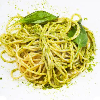 spaghetti mixed with pesto and basil leaf on white plate close up