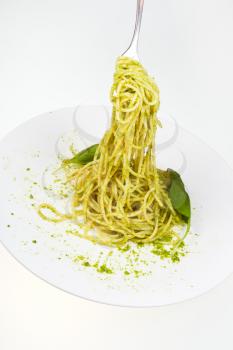 eating spaghetti mixed with pesto from white plate