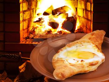adzharia hachapuri with egg on plate and open fire in wood burning stove