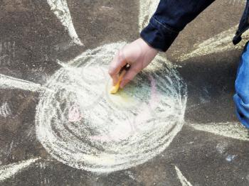 girl paints a sun with colored chalk on asphalt outdoors