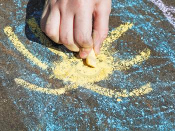 girl drawing yellow sun in blue sky with colored chalk on pavement on street
