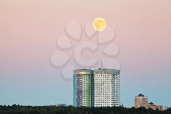 full moon in pink sky over urban houses in summer evening