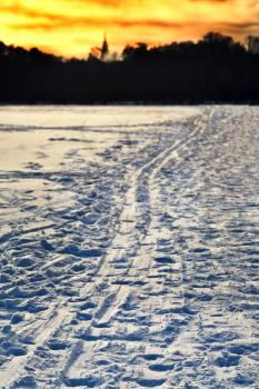 cold yellow winter sunset over ski trails in snowy field