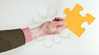 yellow puzzle piece in male hand on grey background
