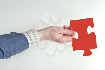 male hand holding red puzzle piece on grey background