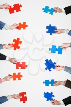 set of red and blue puzzle pieces in opposite sides in people hands on grey background