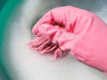 hand in pink rubber glove rinsing wet cloth in foamy water