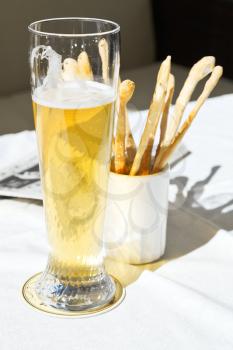 glass of beer and bread sticks on table at outdoor restaurant